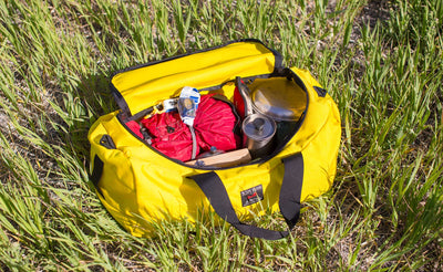 lifestyle  visible^^Canary (yellow) 1000d Cordura Large Yeoman filled with camping gear, laying in the grass.