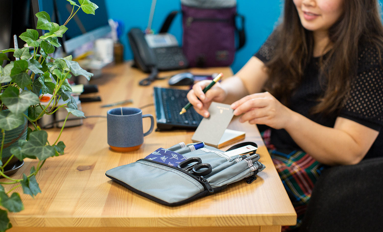 visible lifestyle^^A person sits at their office desk. In the background is an Aubergine Cafe Bag. They are working out of a Small Cafe Bag Freudian Slip in Cloud.