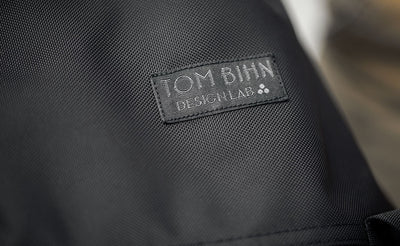 detail visible^^The Shadow Guide has the TOM BIHN Design Lab label; the label is rectangular, smaller than our original label, and has a black background with dark grey text in the foreground. The three dots are the Therefore sign.