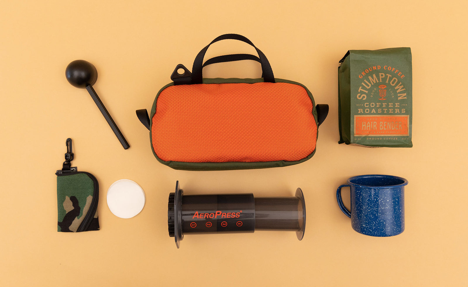 detail visible^^ A Texturized Orange Grab Bag surrounded by travel coffee making items. 