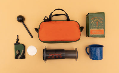 detail visible^^ A Texturized Orange Grab Bag surrounded by travel coffee making items. 