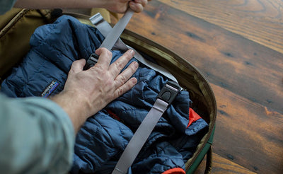 detail visible^^A person lashing down a padded jacket the main compartment of the Guide's Edition Synik 22 using the included tie-down straps.