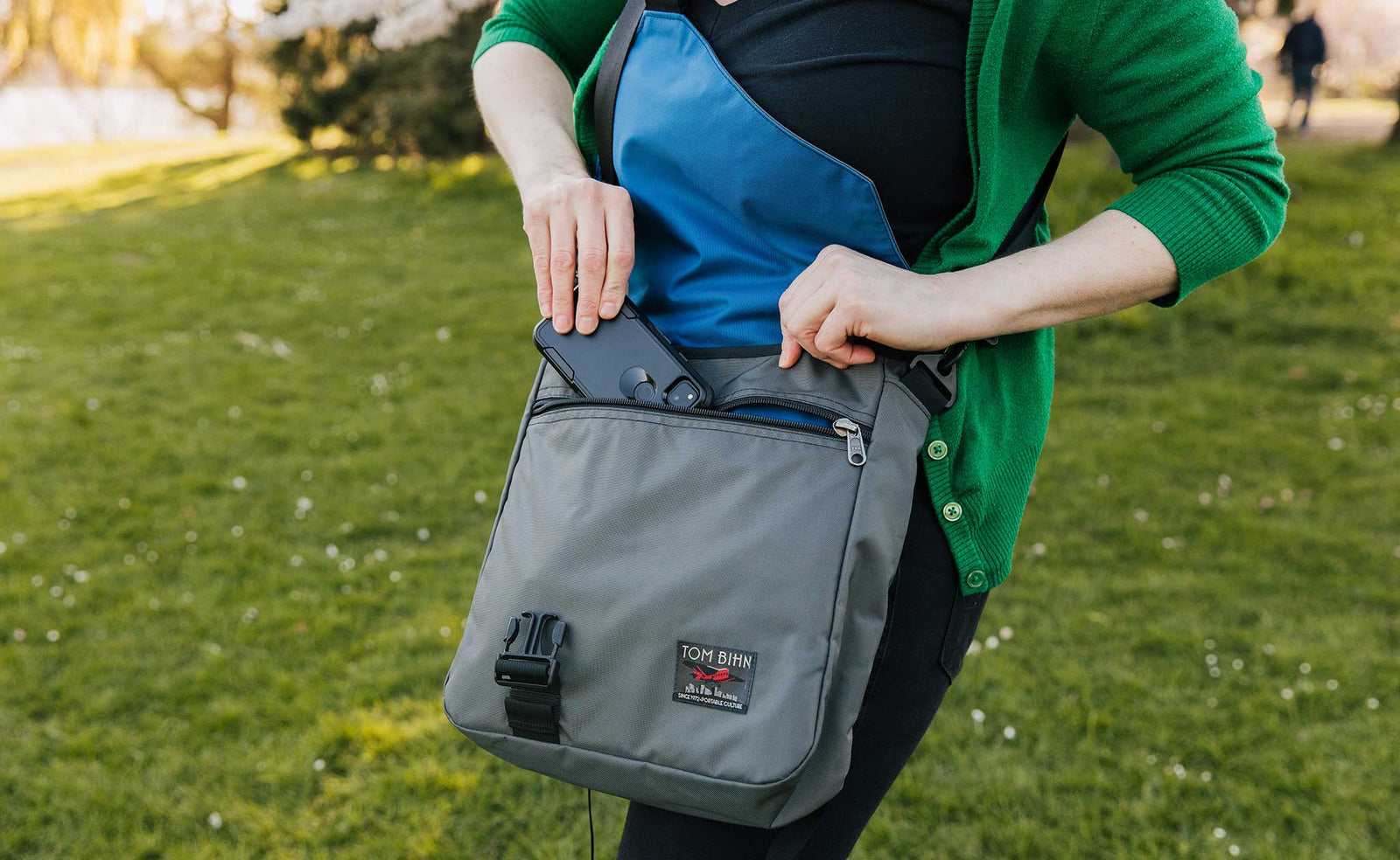 lifestyle visible^^Person walking in a park while wearing the Large Cafe Bag. Pulling a phone out of the front zipper pocket.