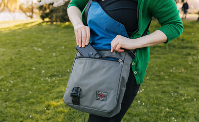 lifestyle visible^^Person walking in a park while wearing the Large Cafe Bag. Pulling a phone out of the front zipper pocket.