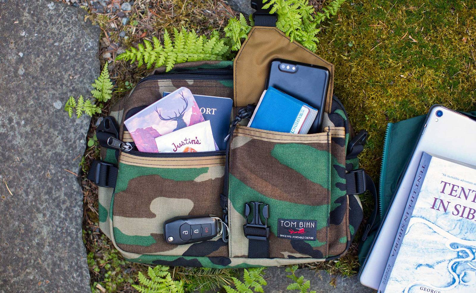 lifestyle visible^^Photo of the LGD in Beaver Camo 1000d. Various items are in it and around it; passport, large phone, wallet, the book "Tent Life in Siberia" and an 11" iPad.