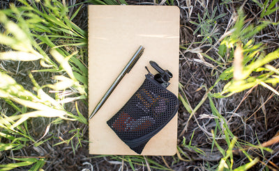 A closed Super Mini Ghost Whale Pouch on a notebook, outside on a patch of grass.