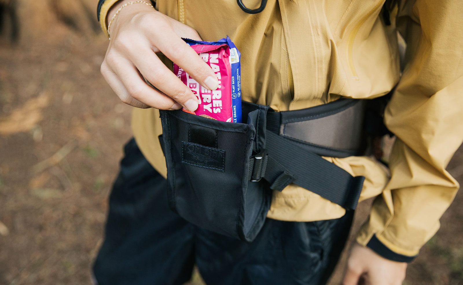 lifestyle visible^^Person putting a nature bar in the Padded Hip Belt Pocket.