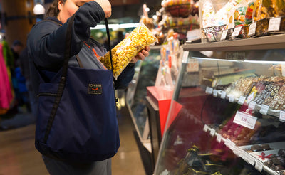 lifestyle visible^^A person putting a sealed bag of popped popcorn in the main compartment of the Pop Tote.