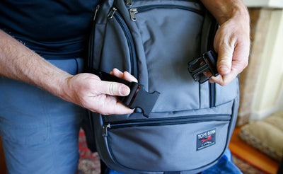 detail visible ^^ A person about to clip the Simple Rolling Luggage Strap around a Synapse backpack.