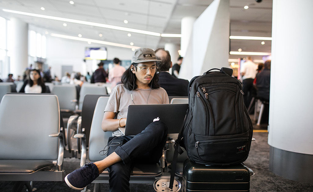 lifestyle visible^^A person working on their laptop on an airport while their Synik 30 sits on their roll-aboard luggage.