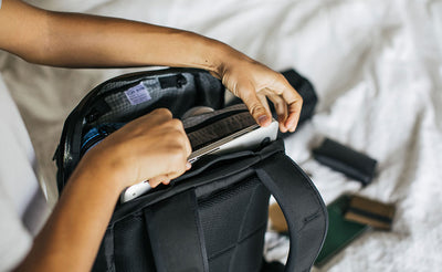 ^^A person sliding their laptop into place in the Synik 30's laptop compartment via the main pocket's zipper.