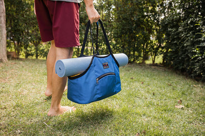 lifestyle visible^^Person carrying the Truckasana yoga tote with a yoga mat cradled in it. They are outdoors on green gass.